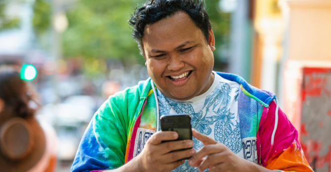 A young man in a bright t-shirt, smiling and looking at his smart phone